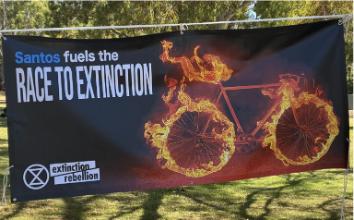 Zdjęcie transparentu z napisem „Santos napędza wyścig ku wymieraniu” zlogo XR i rowerem w płomieniach.
